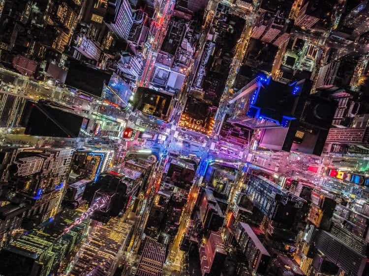 Overhead shot of buildings and streets around Times Square. Advertisements and displays glowing colourful light. Manhattan, New York City, USA