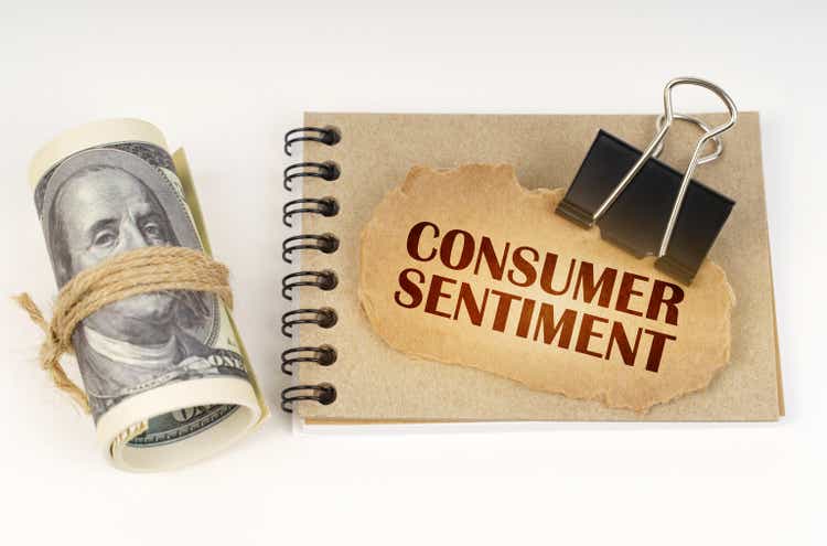 On a white surface are twisted dollars, a notebook and a cardboard sign with the inscription - Consumer Sentiment