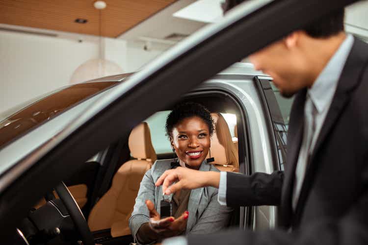 Mature woman talking to the car salesman about a car purchase while checking out the car