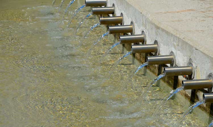a series of stainless steel pipes emerge from the concrete dam and clear water flows out of them in a stream. aeration of stagnant water for fish breeding in the pond, steel, metal, gray