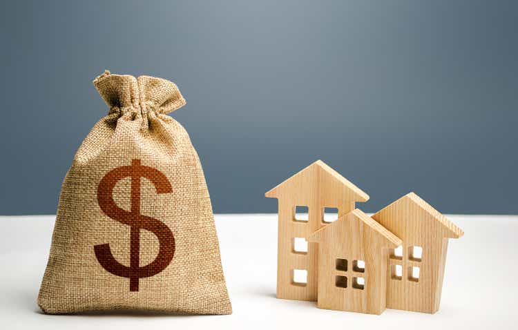 Dollar money bag and figurines of residential buildings. Mortgage loan. City municipal budget. Investment in real estate. Costs of service and maintaining buildings. Purchase of housing. Property tax