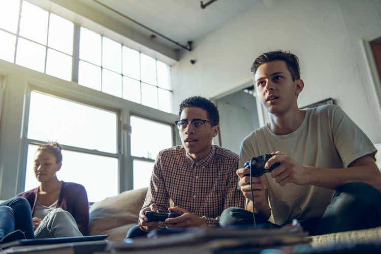 Young men playing video game sitting by female friend in living room