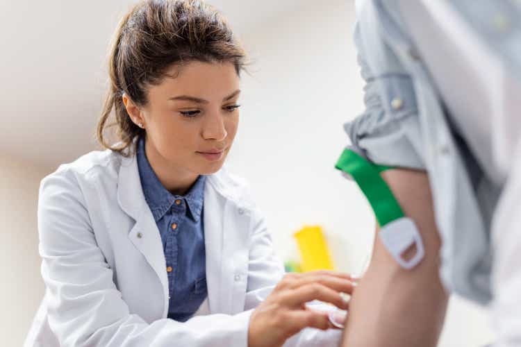 Friendly hospital phlebotomist collecting blood sample from patient in lab. Preparation for blood test by female doctor medical uniform on the table in white bright room