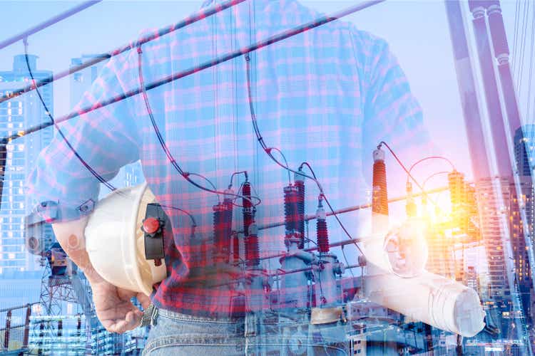 Double exposure of engineer, holding safety helmet and a power plant construction drawing in the cit