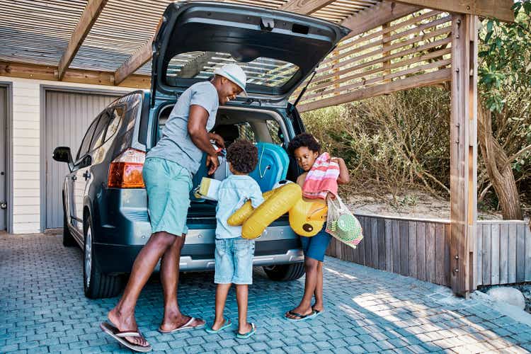 A family packing the car to leave for summer vacation. A happy african american father and his two cute little sons preparing the luggage in his vehicle to go on a road trip, ready for travel time