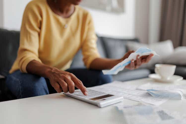 Close-up of a middle-aged woman sitting in the living room at home and checking her electricity bill. She has a worried look on her face.