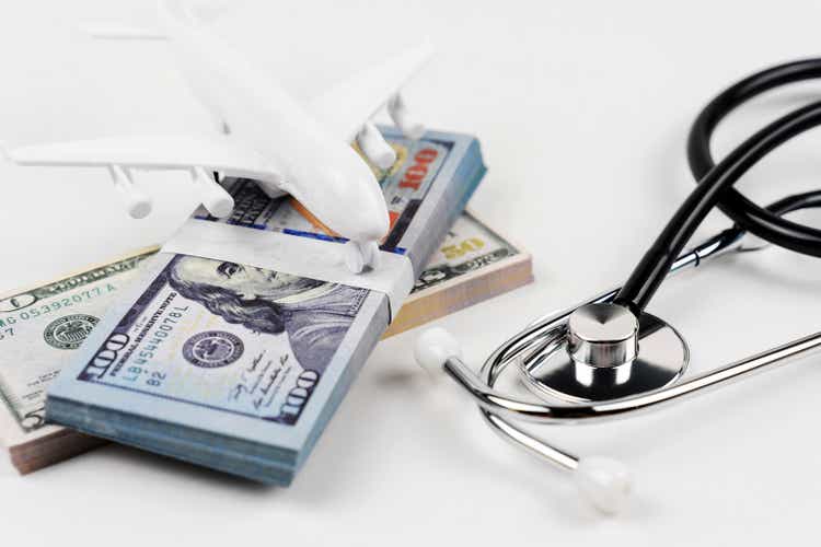 Stethoscope and mini airplane on top of stack of money