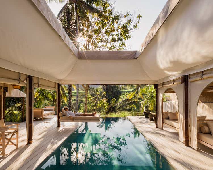 Asia, Indonesia, Bali, young man relaxing on swing bed, suspended over salt water pool at Eco friendly, tented luxury Glamping resort.