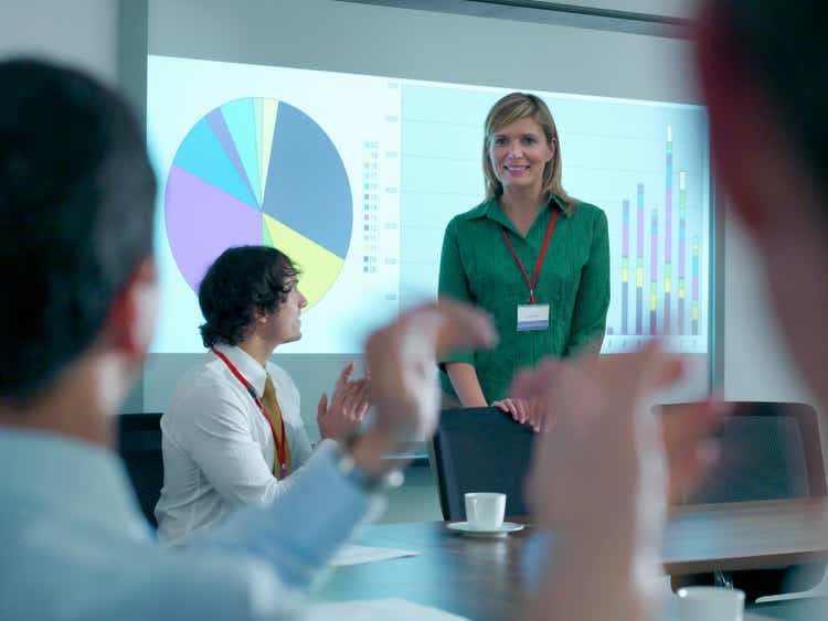 Businesswoman congratulated by colleagues in conference room for smart board presentation