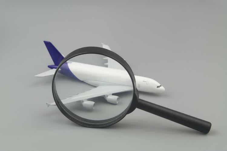 Airplane model under magnifying glass and calculator on gray background