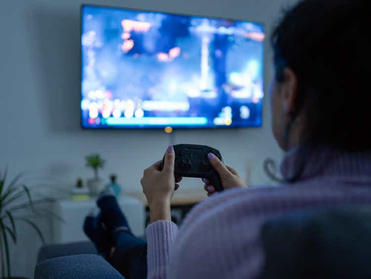 Woman playing video games with a wireless joystick in the tv room.