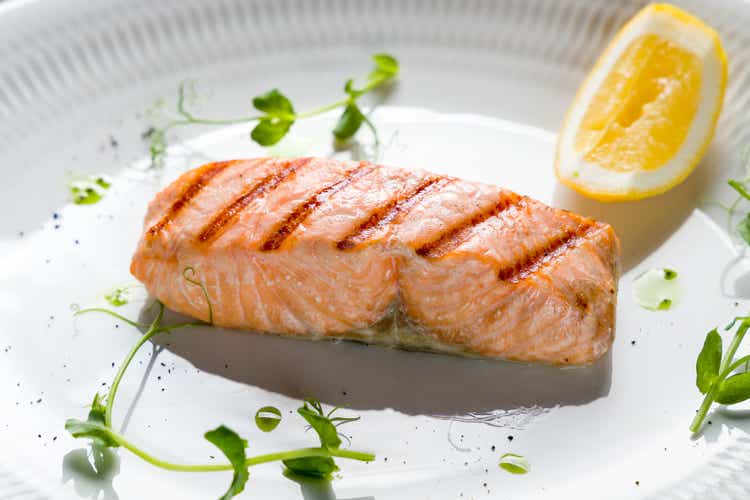 Salmon steak on the grill with greenery and lemon on a white plate with reflection macro close up