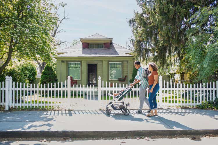 Young mother and father walking with baby daughter in stroller on neighborhood sidewalk