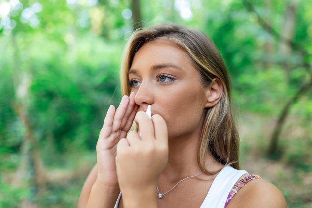 Mujer que usa aerosol nasal al aire libre para el tratamiento de la alergia al polen de árbol