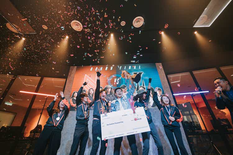 Asian Esports team holding trophy mock up cheque celebrating victory cheering winning grand final videogame on stage. Videogame Championship Arena. Cyber Games Tournament Event
