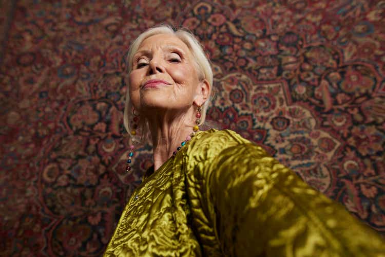 Elderly woman against wall hanging rug