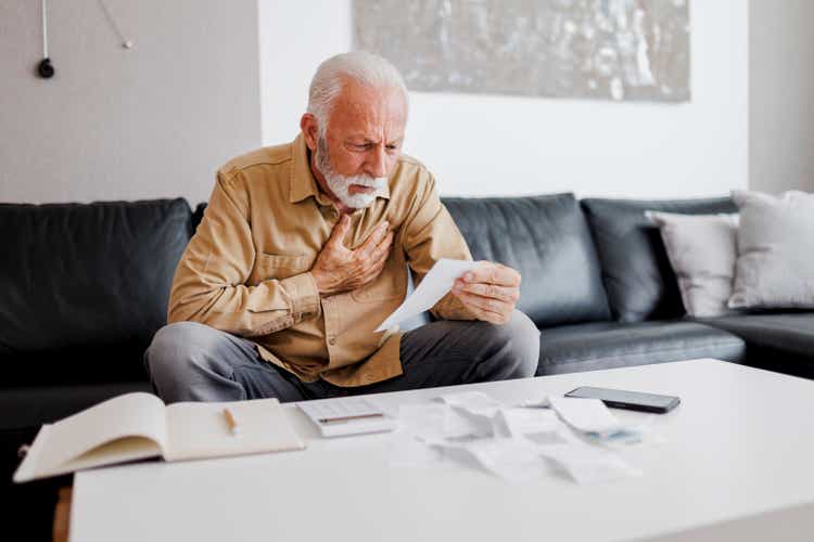 Shot of a senior man suffering from chest pain while checking bills and sitting on the sofa at home