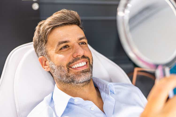 Middle aged man reviewing wrinkles in hand mirror.