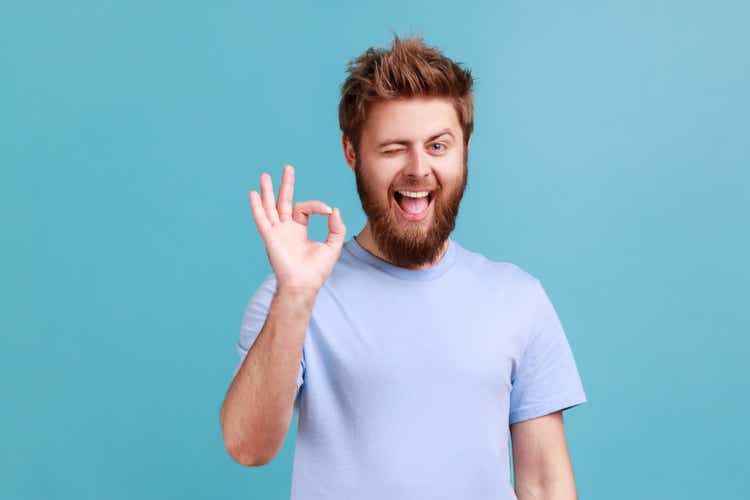 Man in blue T-shirt showing okay sign, success sign, satisfied with good service, looking at camera.