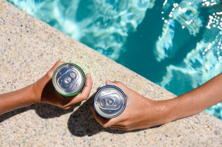 Two hands hold cans of cold drink in the pool on a hot day. The concept of vacation in a friendly company.