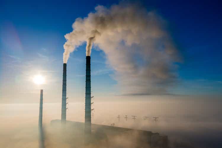 Aerial view of coal power plant high pipes with black smoke moving up polluting atmosphere at sunset.