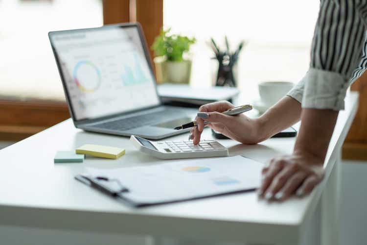 Close up Business woman using calculator and laptop for do math finance on wooden desk, tax, accounting, statistics and analytical research concept