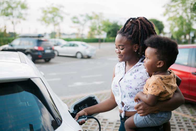Mother holding her son while charging her electric vehicle