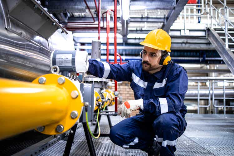 Refinery blue collar worker standing by LPG pipeline and checking gas production or distribution.