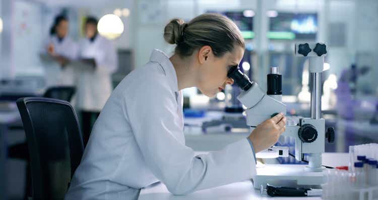 Serious, focused and determined scientist working with a microscope in a modern lab at night. Busy research biology tech specialist analyzing sample tests with advance laboratory technology equipment