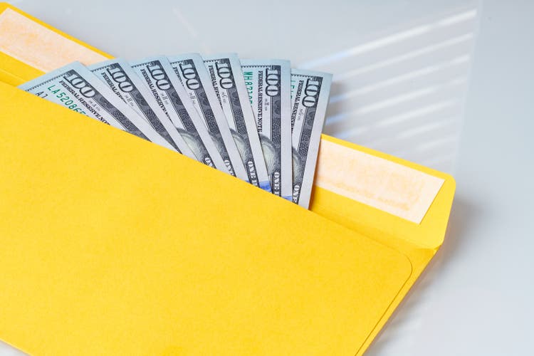 Yellow envelope with dollar bills on white table. Open envelope containing dollar banknotes. Symbol of profit in business. Unlegal wealth and income. Bribe and corruption.