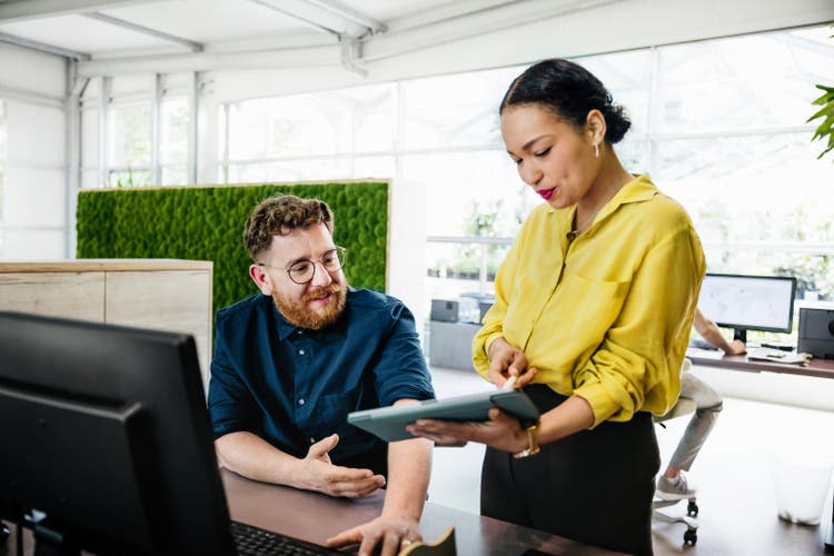 Office Manager Showing Documents On Digital Tablet To Colleague