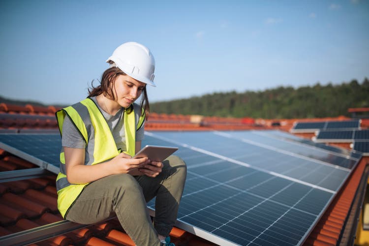 Female engineer sitting on a rooftop with solar panels using technology.