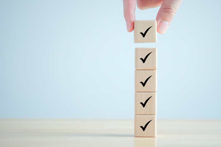 Checklist, Task list, Survey and assessment. Quality Control. Goals achievement and business success. Hand holding Check mark on wooden blocks for complete check list.