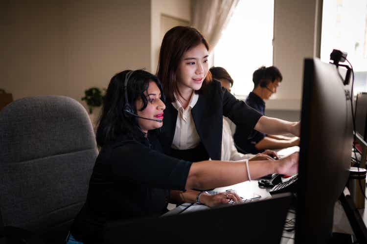 Female customer support representatives wearing headsets and working late at work desk in call center