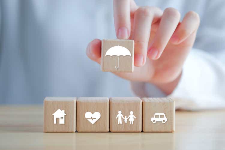 Insurance concept. Protection against a possible eventuality. Hand holding umbrella icon and House, Car, Family and Health icon on wooden block for assurance life concept.