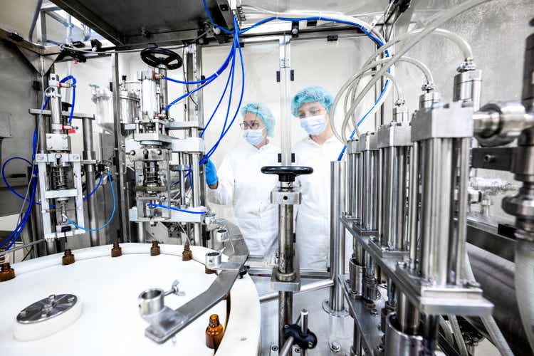 Two female employees in a pharmaceutical laboratory seen while controlling the process of drugs manufacturing