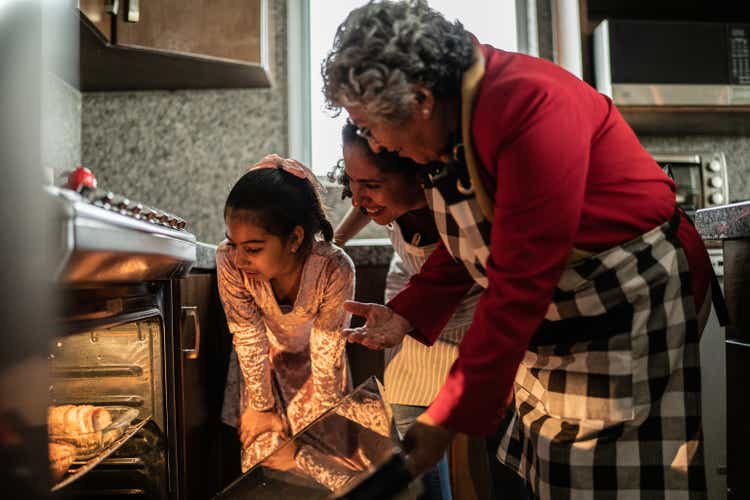 Grandmother, mother and daughter looking at food in the oven at home