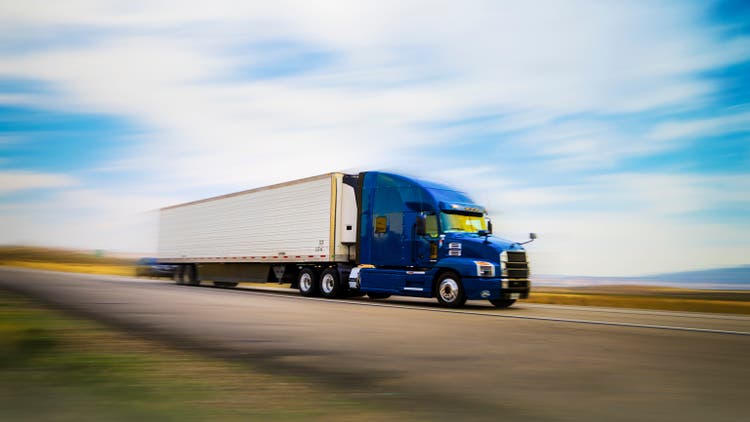 Blue and white semi-truck transporting merchandising at sunset - motion blur