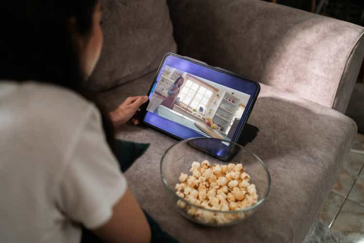 Over the shoulder device screen of Woman watching comedy movie streaming on digital tablet at home.