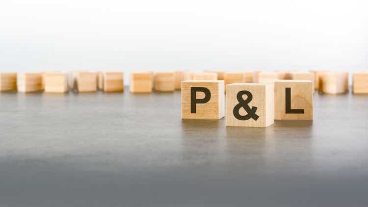 three wooden blocks with letters P and L - profit and loss - with focus to the single cube in the foreground in a conceptual image on grey background