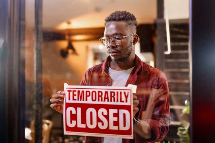 Cropped shot of a man holding up a "temporarily closed" sign in his store