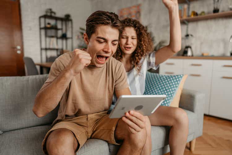 Young Couple Watching A Sports Game On Tablet And Rooting For Their Team