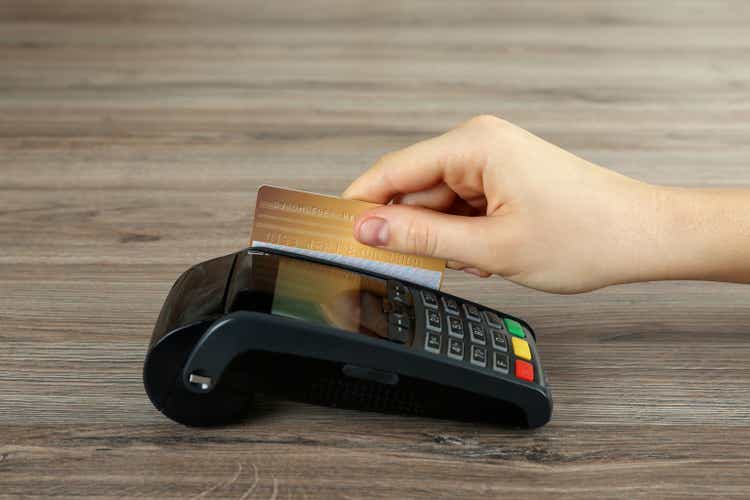 Woman with credit card using modern payment terminal at wooden table, close up