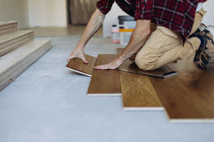 The man is installing the wooden plank of the parquet floor