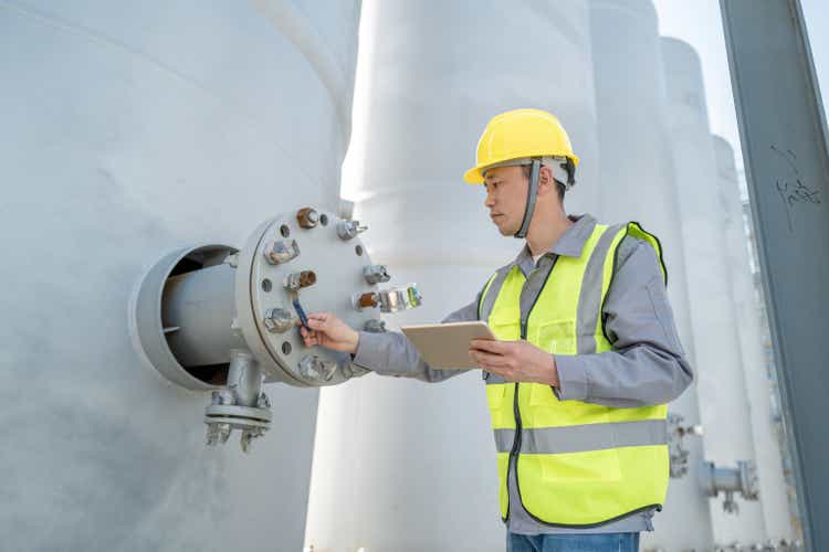 An Asian male worker brought in a tablet computer to inspect chemical equipment at a chemical factory.