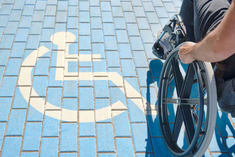 unrecognizable handicapped man in a wheelchair passing over handicapped sign painted on the ground