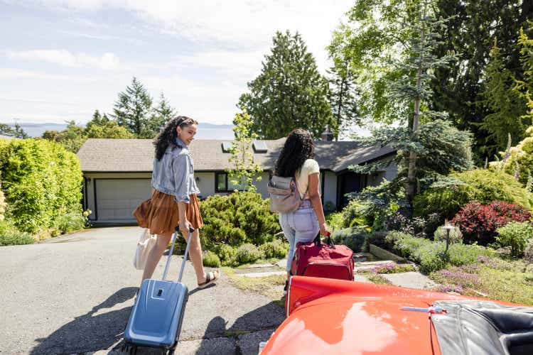 Young women friends with suitcase walking toward vacation house rental