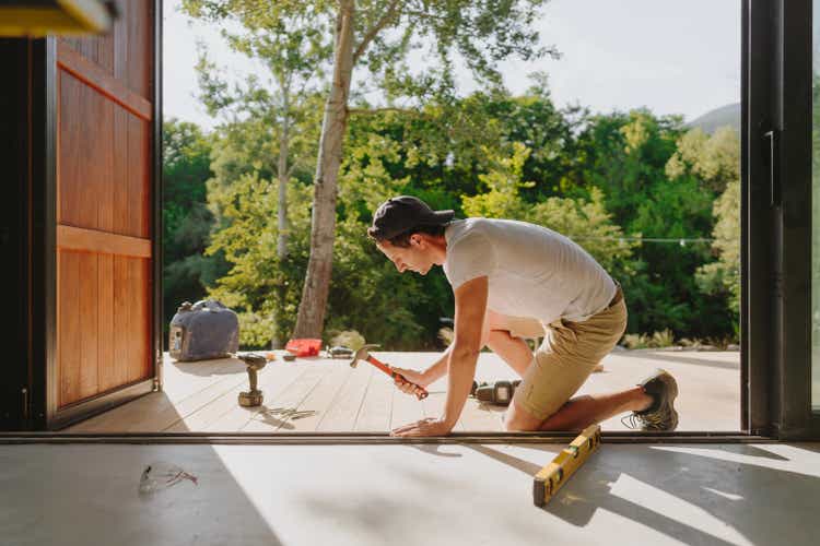 Man working on wooden decking in front of a cabin house