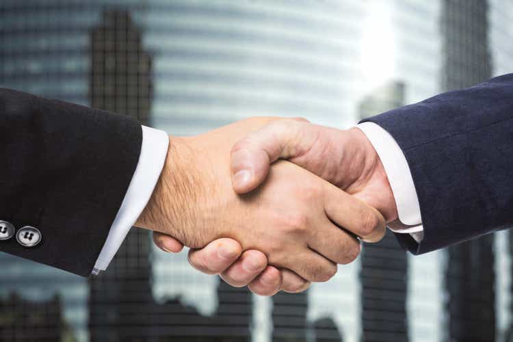 Two businessmen shake hands on the background of office building windows, partnership concept, close up