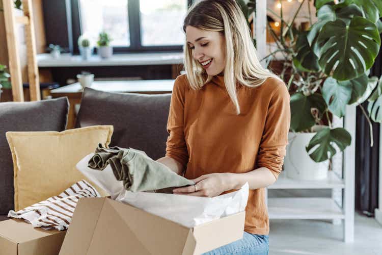 Smiling young woman unpacking parcel while sitting on couch at home